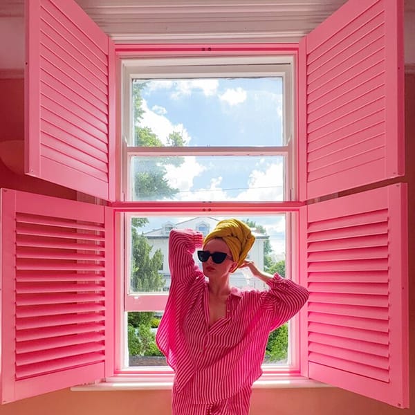 bright window with vivid pink shutters, open slats framing blue sky and a small plant below