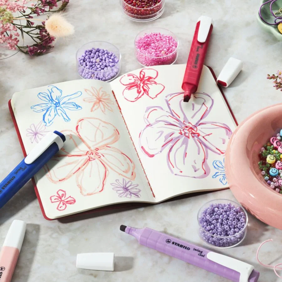 Notizheft mit Blumen und Textmarker in lila, rot und rosa daneben