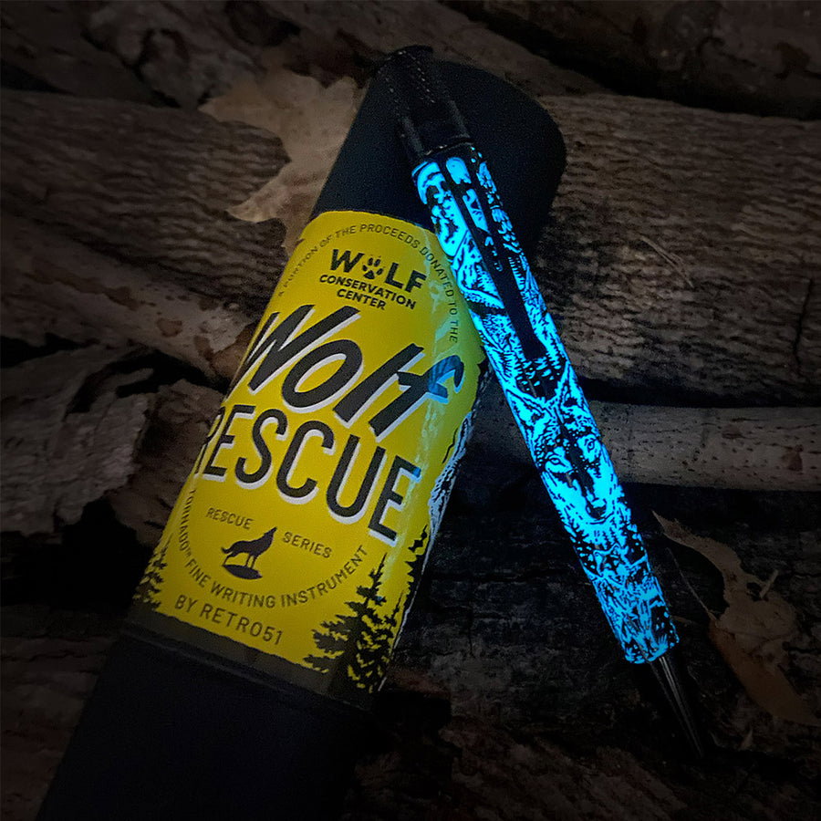 Wolf Rescue pen, glowing in the dark, with its packaging and display tube, lying on some logs.