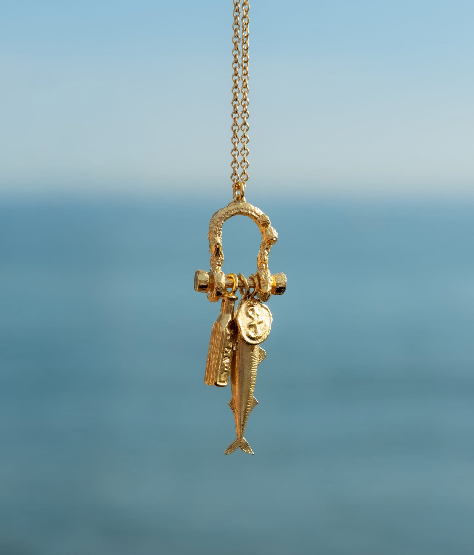 Alex Monroe Gold Mudlark Boatyard Link Charm Necklace from the "By the Sea" collection, set against a blurred ocean background.