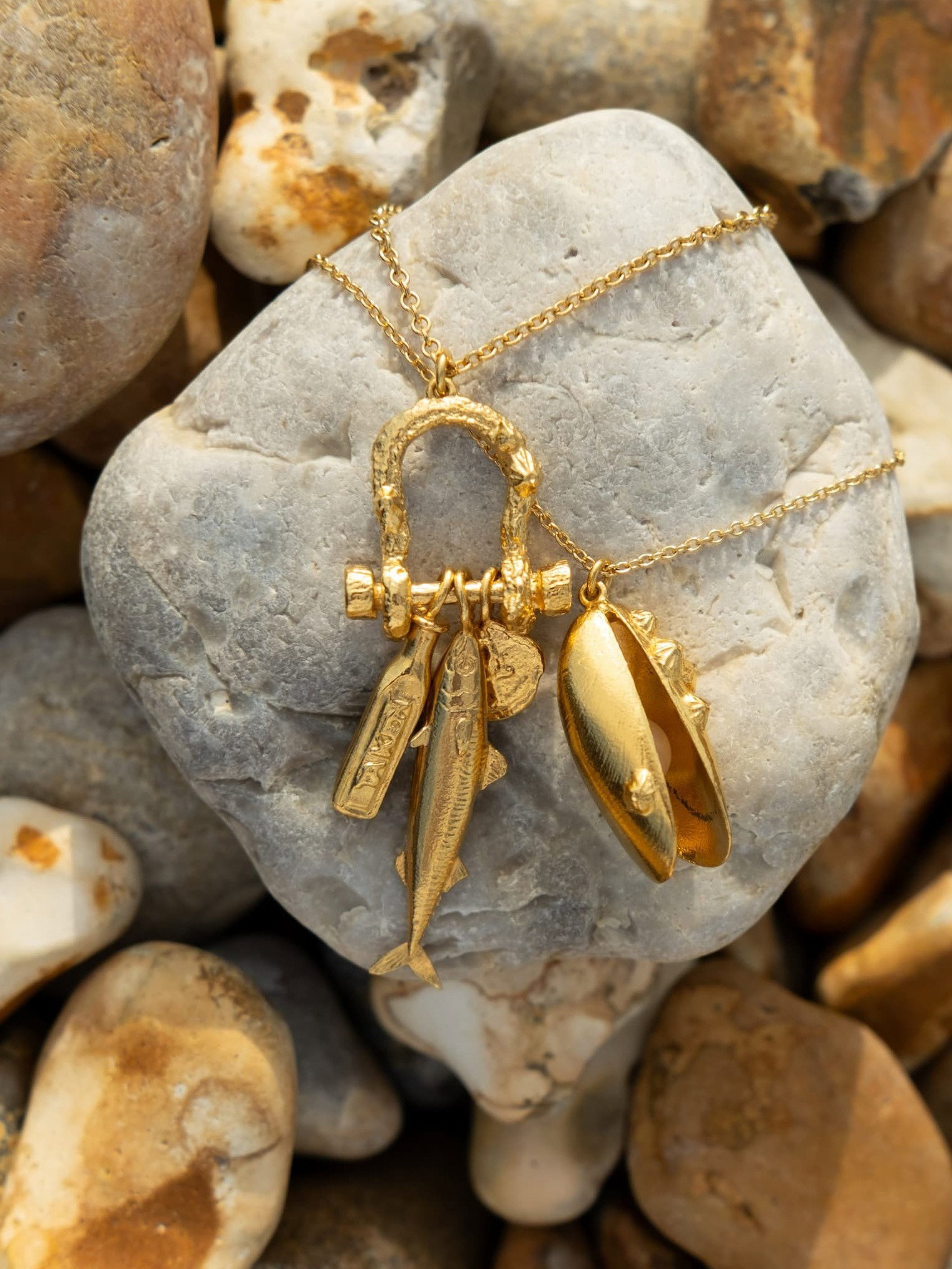 Engraved Shell Necklace in sterling silver displayed on a smooth pebble,  with a natural background of rounded beach stones in warm neutral tones.