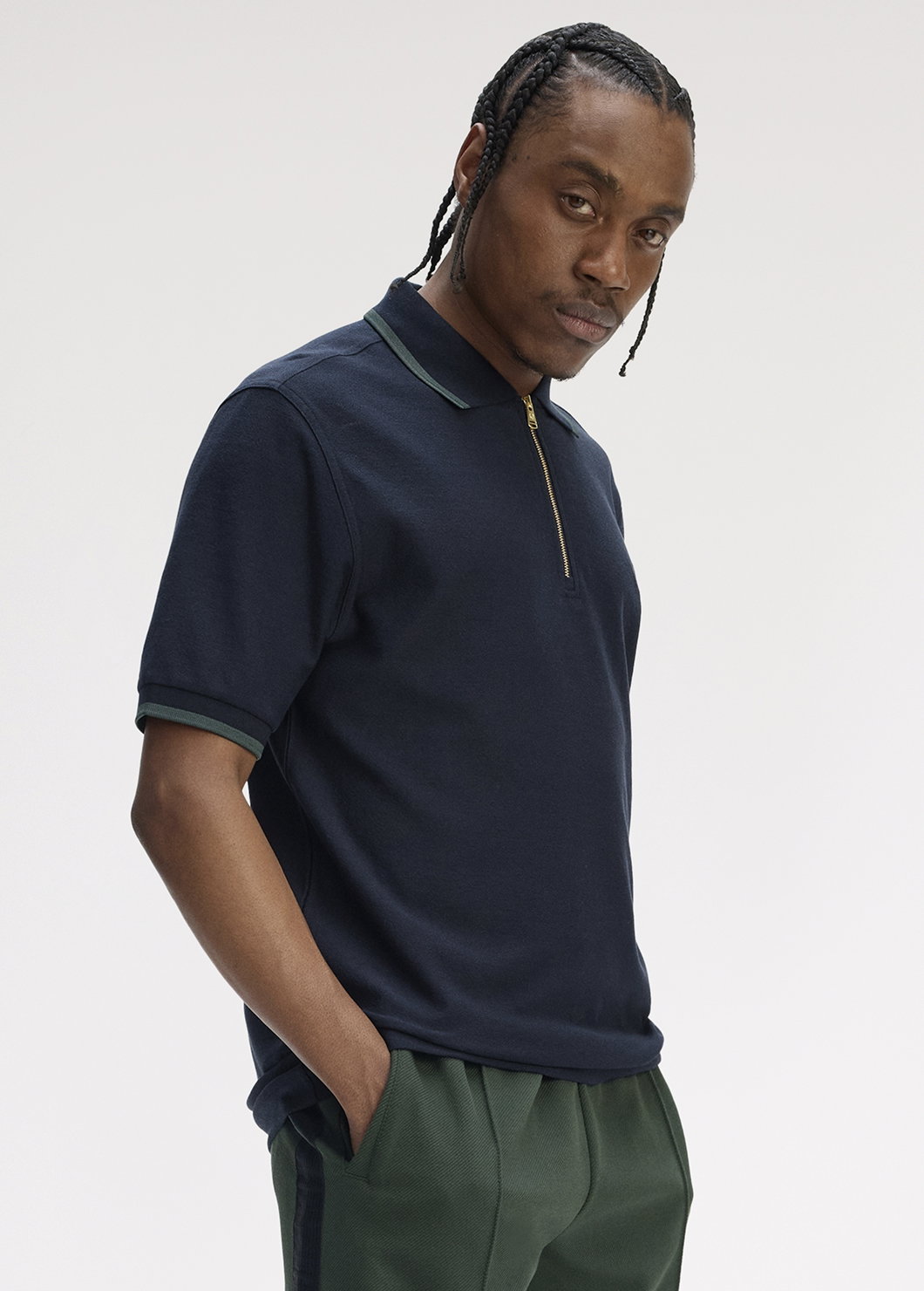 Black male model with braids puts his hands in his pockets and nonchalantly looks into the camera. He wears a navy crepe zip up polo shirt which is currently in the sale