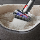 Un minicepillo antienredos Hair screw™ de Dyson limpiando una cama para mascotas.