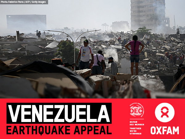 several people are stood amongst the rubble of collapsed buildings; the destruction continues as far as the eye can see.