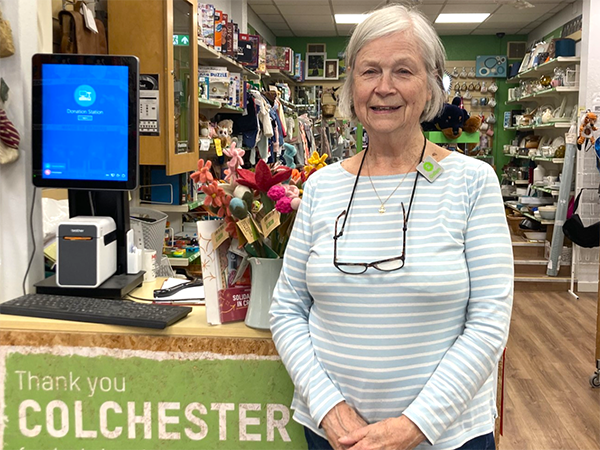 a woman stood in front of a shop till, smiling at the camera.