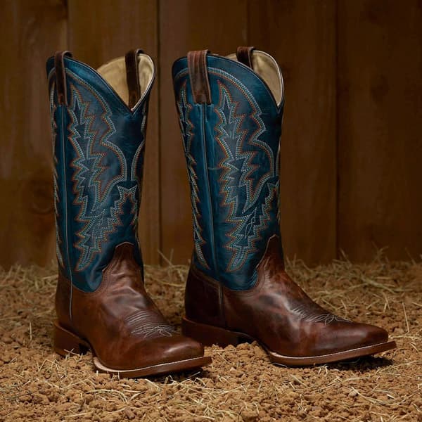 Pair of Tony Lama boots sitting on hay and dirt.