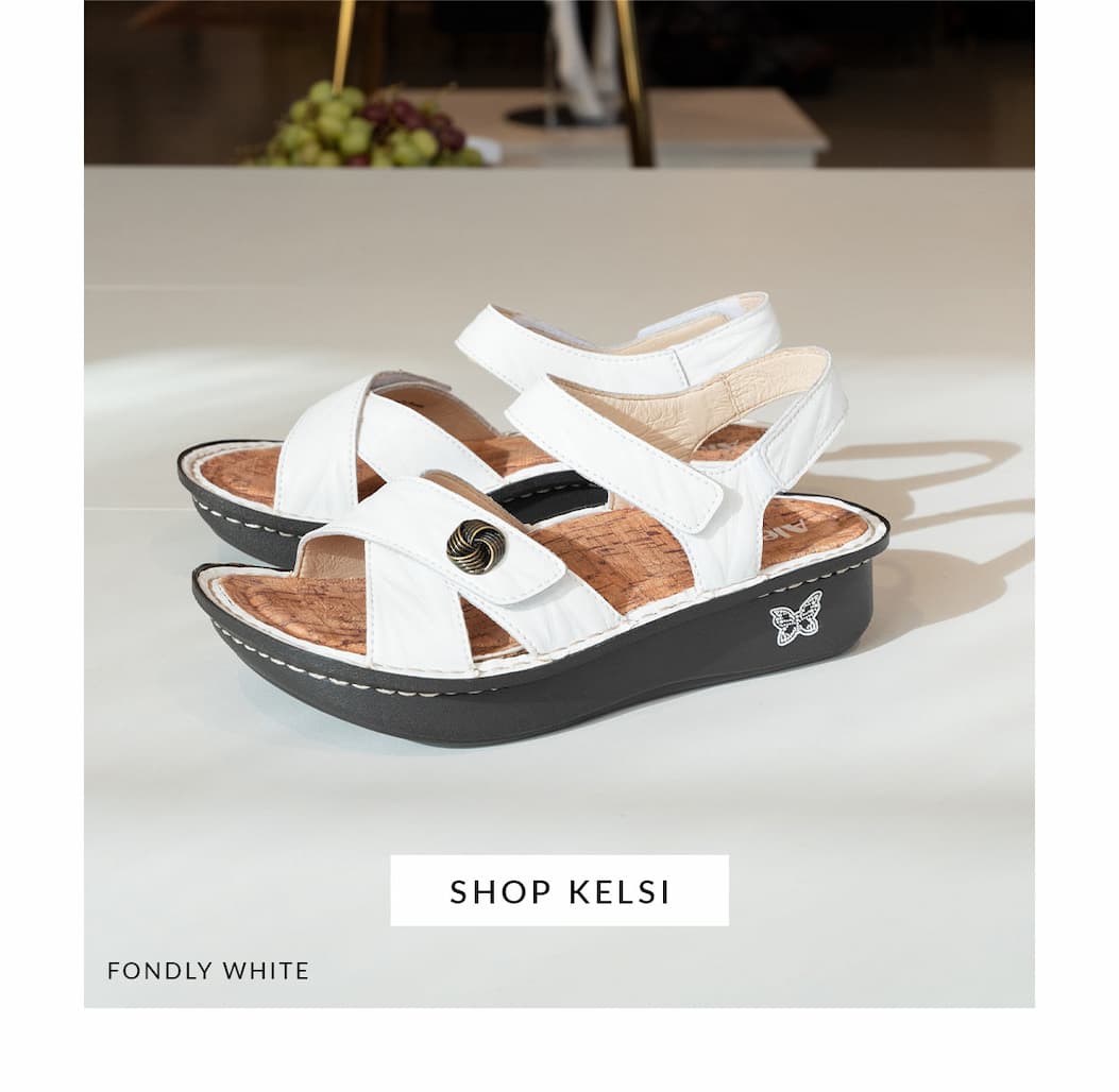White Alegria Kelsi sandals in Fondly White with adjustable hook-and-loop straps, decorative button detail, and a supportive Classic Footbed, displayed indoors.
