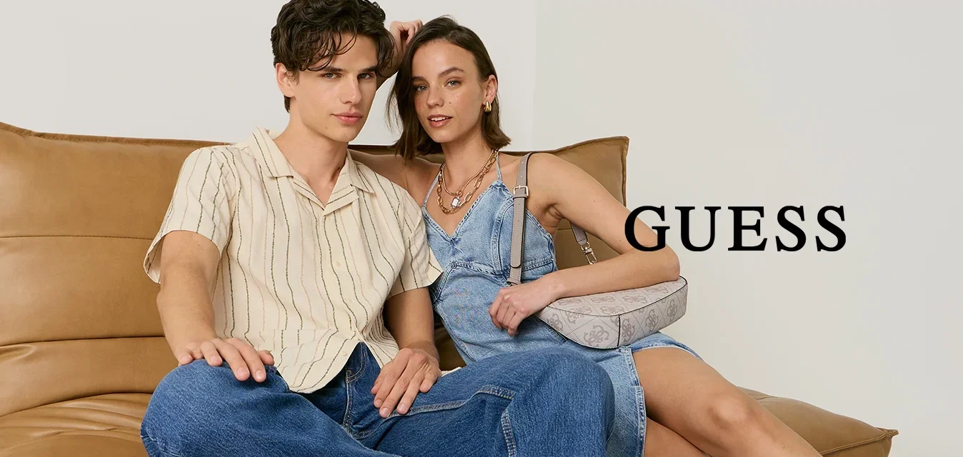 Jeune homme en chemise rayée et jean et jeune femme en robe bleue et talons noirs assis sur un canapé en cuir beige devant un fond uni.