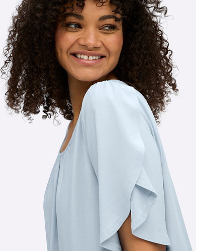 Model in pastellblauem Shirt mit überlappenden Ärmeln.