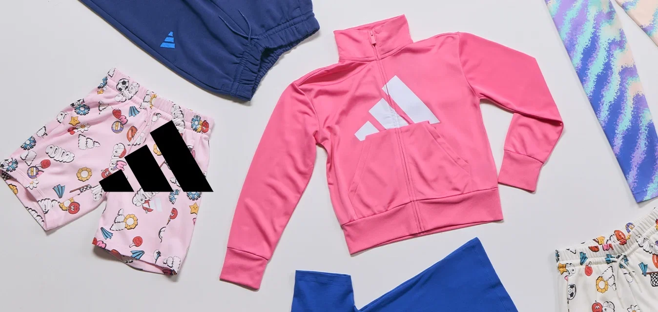 Varios artículos de ropa infantil, incluyendo una chaqueta rosa con cremallera, pantalones cortos con estampado y leggings multicolores, dispuestos sobre una superficie blanca.