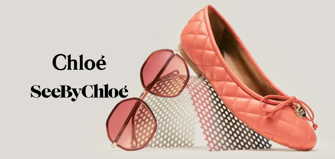 Ballerina trapuntata color corallo con dettaglio fiocco appoggiata su una rete bianca, occhiali da sole con lenti rosa appoggiati alla rete su uno sfondo neutro.