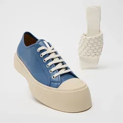 Sneaker in pelle blu con lacci bianchi e una suola spessa beige; accanto, un sandalo a slittamento bianco intrecciato con un tacco curvo.