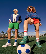 Two men sat on the sidelines of a tennic court in stylish outfits.