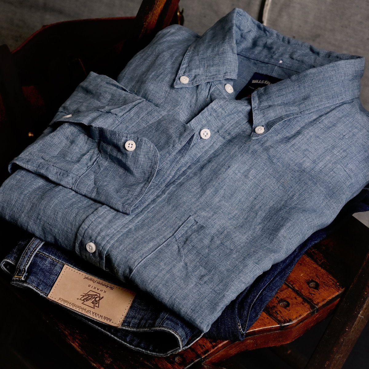 A indigo Blue Khakis standard fit shirt and denim pants sit on a vintage wooden chair
