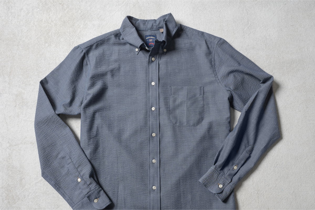 An Indigo toned Bills Khakis standard fit shirt lays on a light colored surface unfolded