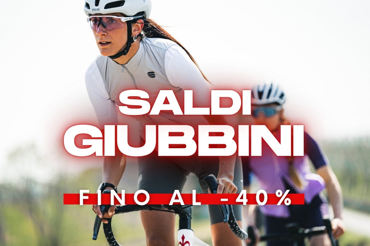 Two cyclists in helmets and cycling jackets riding outdoors with a red promotional overlay reading 'Saldi Giubbini fino al -40%'