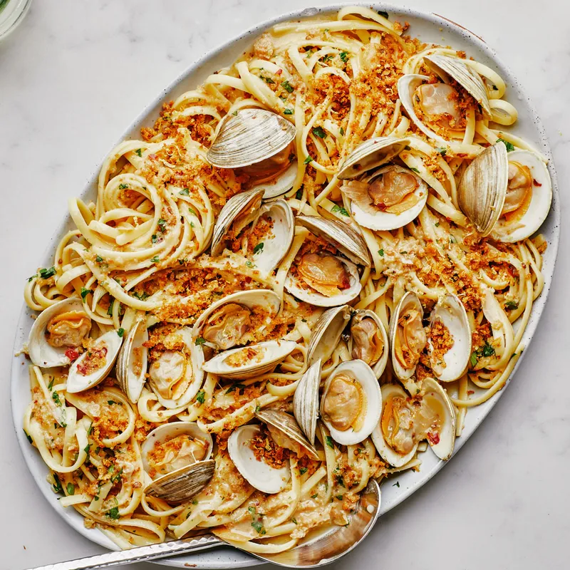 A large platter of linguine with clams alongside a bottle of white wine and two glasses.