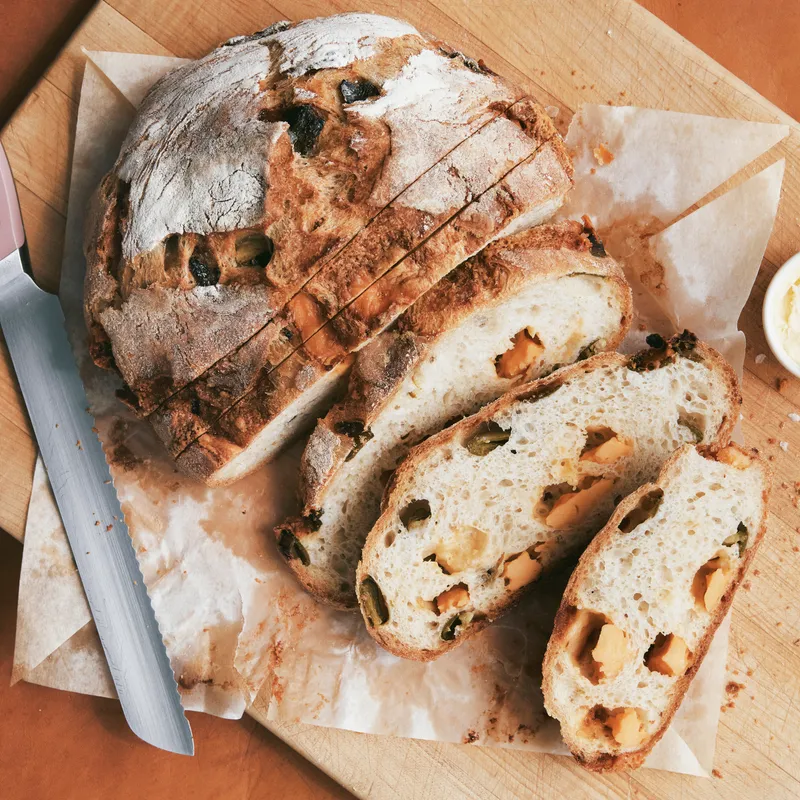 A sliced boule of cheddar jalapeño bread on a cutting board with butter and salt.