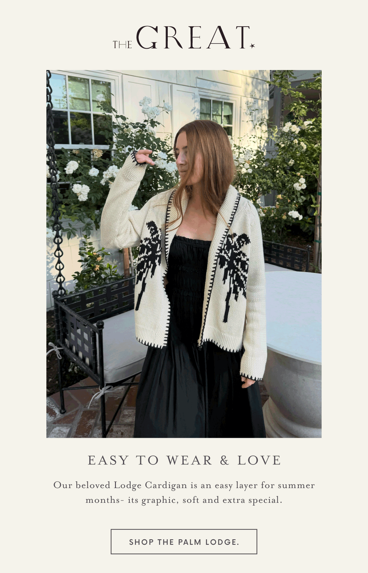 A woman in a black dress and cream cardigan with black palm tree designs stands outdoors near white roses, touching her hair. Text reads: "Easy to Wear & Love" and describes the Lodge Cardigan.
