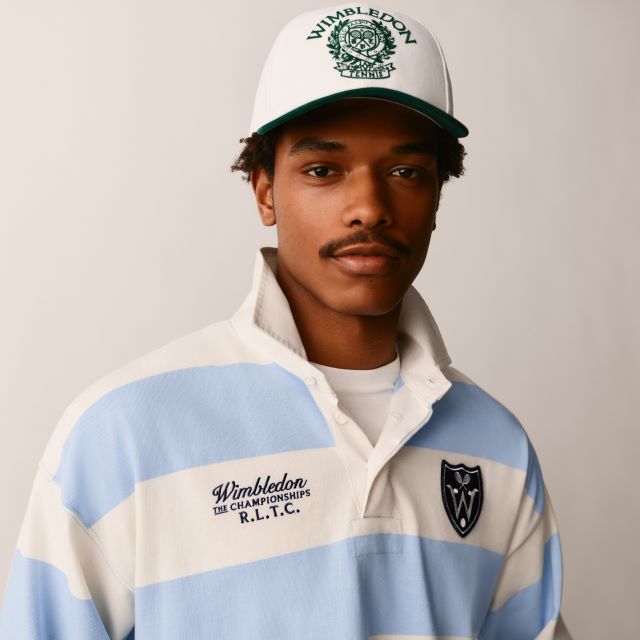 A person wearing a white cap with a Wimbledon logo and a blue and white striped rugby shirt with 'Wimbledon The Championships' embroidery.