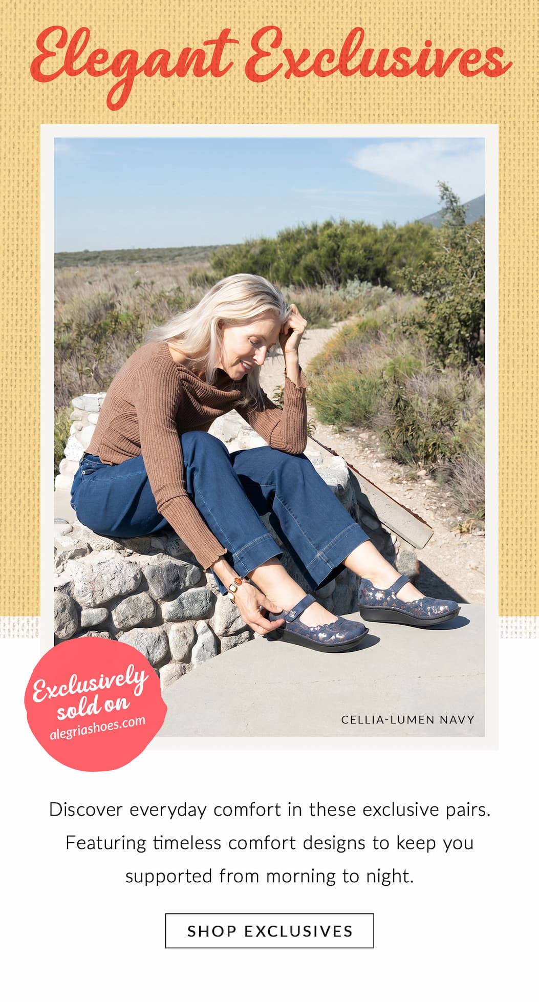 Model is sitting on a rock base with her hand resting on the strap of her Cellia Lumen Navy mary jane.  With a backdrop of vegetation and rocky path in the background.