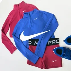 Conjunto de ropa deportiva Nike en rojo y azul que incluye dos camisetas con cremallera hasta el cuarto, leggings a juego y un par de zapatillas deportivas azules sobre fondo blanco.