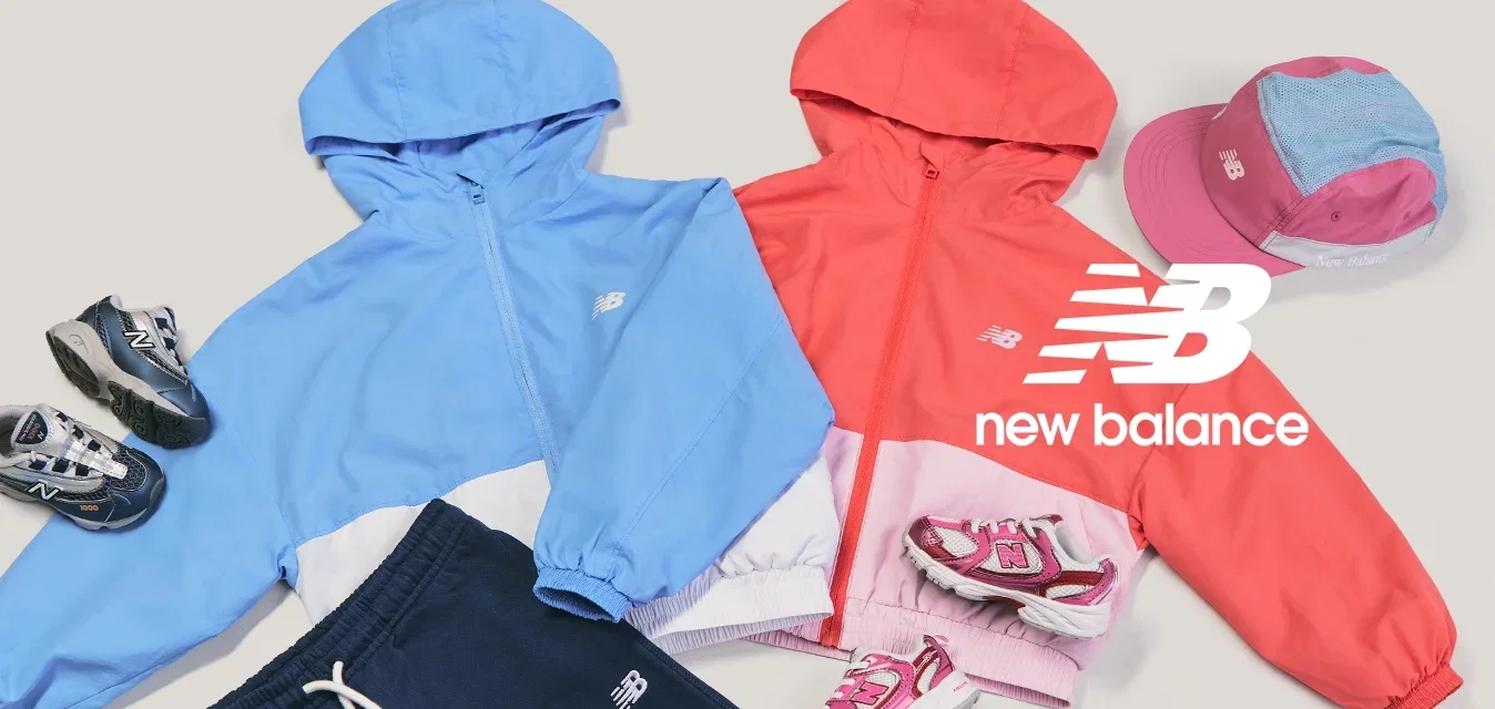 Dos chaquetas con capucha para niños en azul y rojo, acompañadas de gorras a juego, zapatillas deportivas y pantalones azul marino, dispuestas sobre un fondo claro.