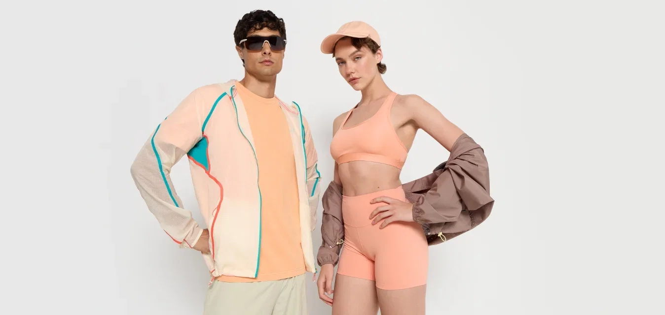 Ropa deportiva que incluye una chaqueta de melocotón claro con detalles azules, combinada con un top corto de melocotón y pantalones cortos, además de una camisa de manga larga oversized de color beige con botones.