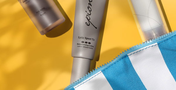 Sunlit Epionce products with natural leaf shadows, spilling out of a blue and white striped cosmetic bag