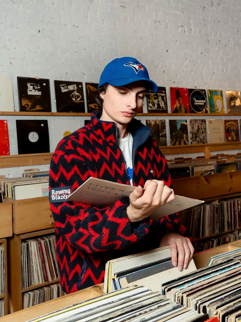 Image may contain: Finn Wolfhard, Baseball Cap, Cap, Clothing, Hat, Person, Teen, Furniture, Face, Head, and Bookcase