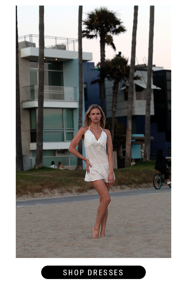 Model on the sand wearing a white mini dress. Shop dresses. 