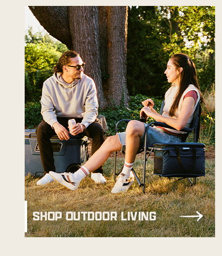 Two people sitting outdoors near a tree, relaxing on camping chairs with cooler bags nearby. Shop outdoor living button with arrow.