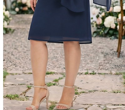 Model in knielangem marinefarbenem Chiffonkleid vor einer Hochzeitskulisse.
