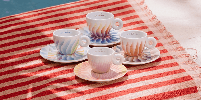 Four colorful espresso cups and saucers arranged on a striped beach towel