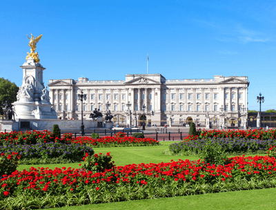 Buckingham Palace surrounded by vibrant flower beds and a clear blue sky.