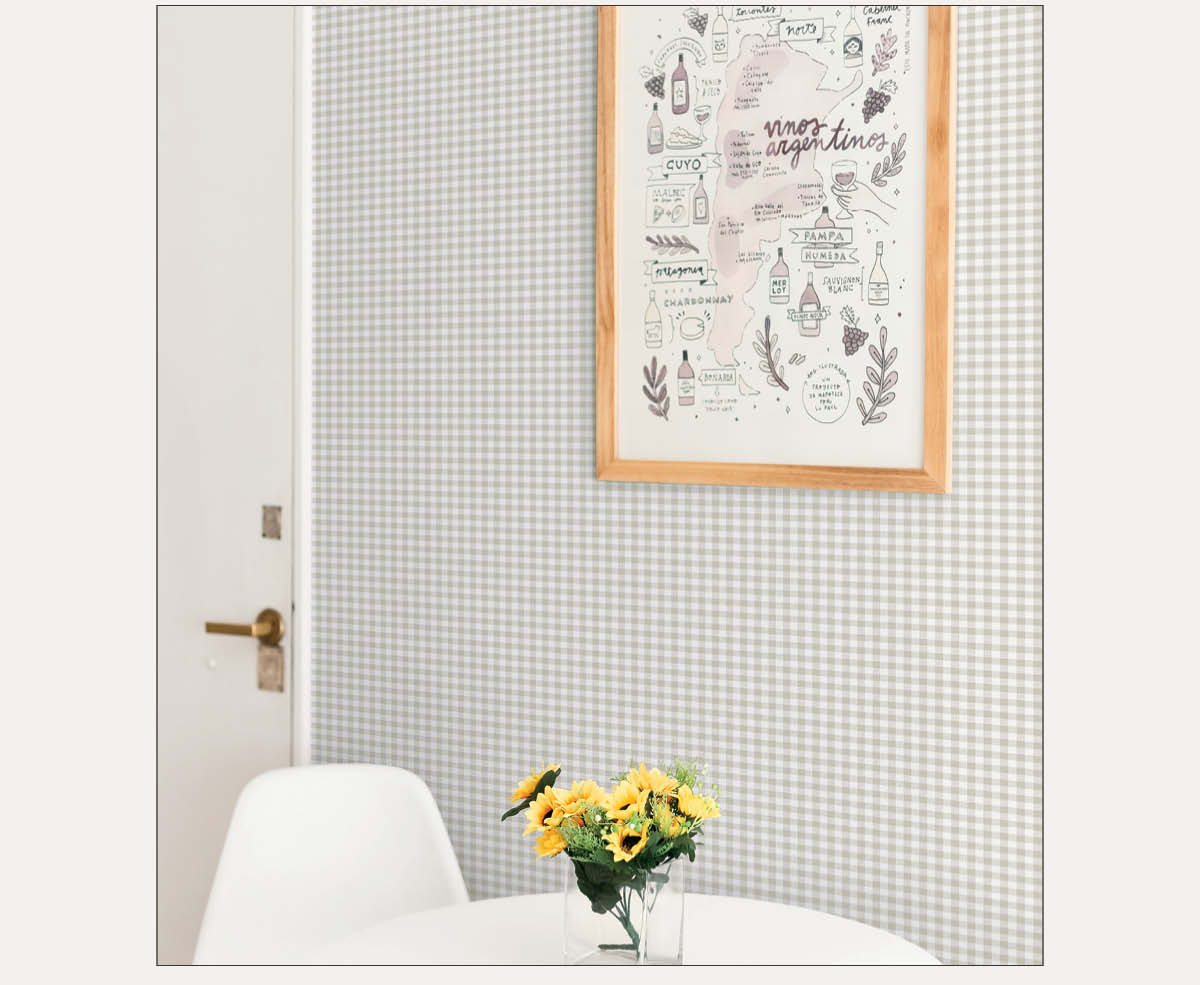 Image of Tempaper's Gingham plaid wallpaper on a wall with a framed picture. Part of a table with a vase with yellow flowers can been seen.