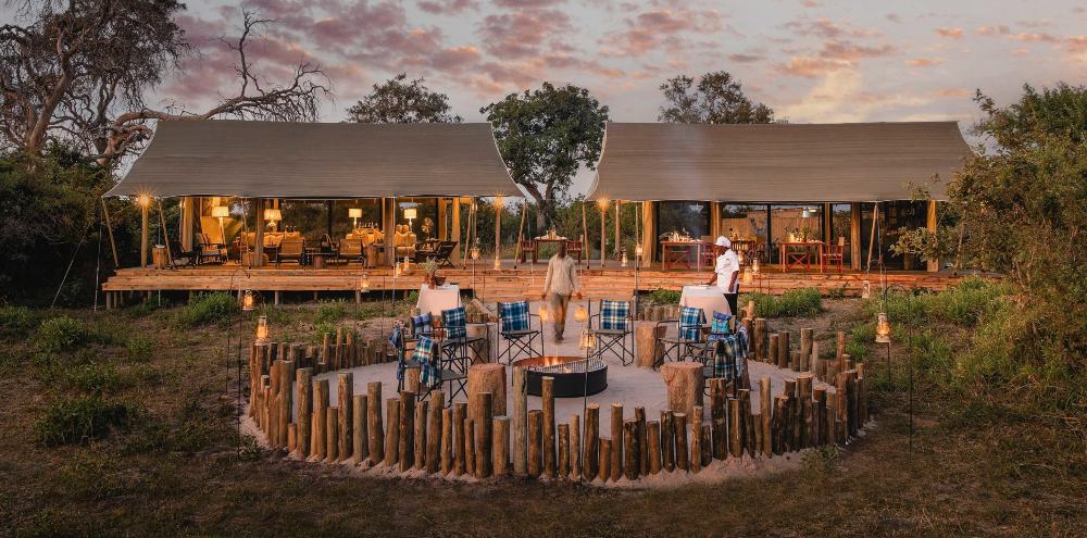 Luxury safari camp with a central campfire beneath the African sunset