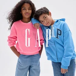 Deux enfants se tiennent ensemble ; une fille en sweat-shirt rose et jean large, un garçon en sweat à capuche bleu GAP et jean, appuyant sa tête sur l'épaule de la fille.
