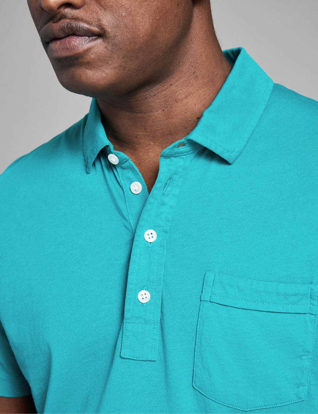 Model wears a teal polo on a grey background.