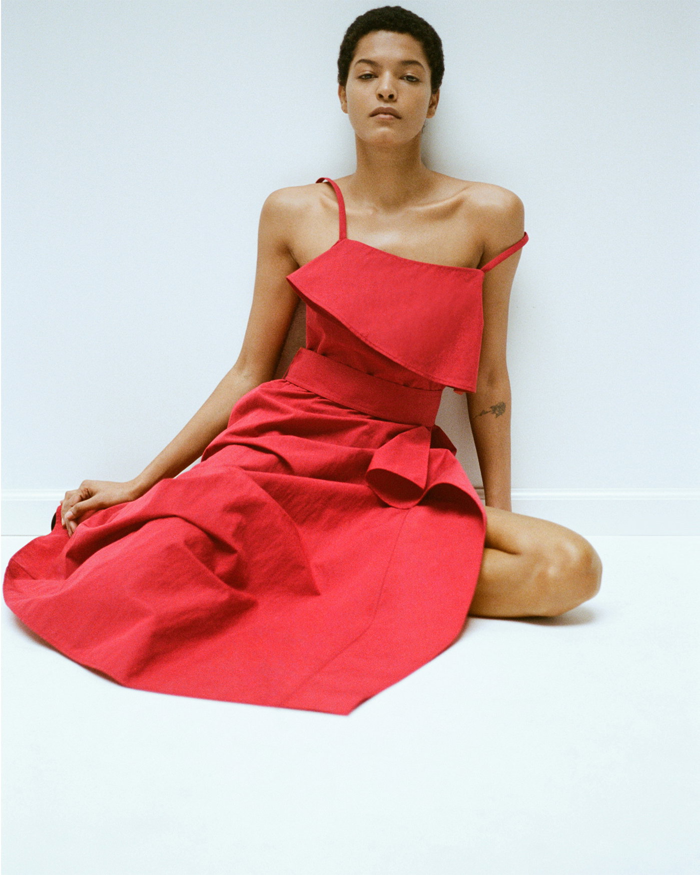 Model sitting against white wall wearing the Reign Dress in Washed Cotton in Brick