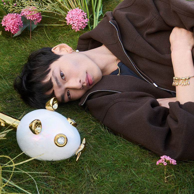 Model lies on the grass beside a super-sized mouse charm