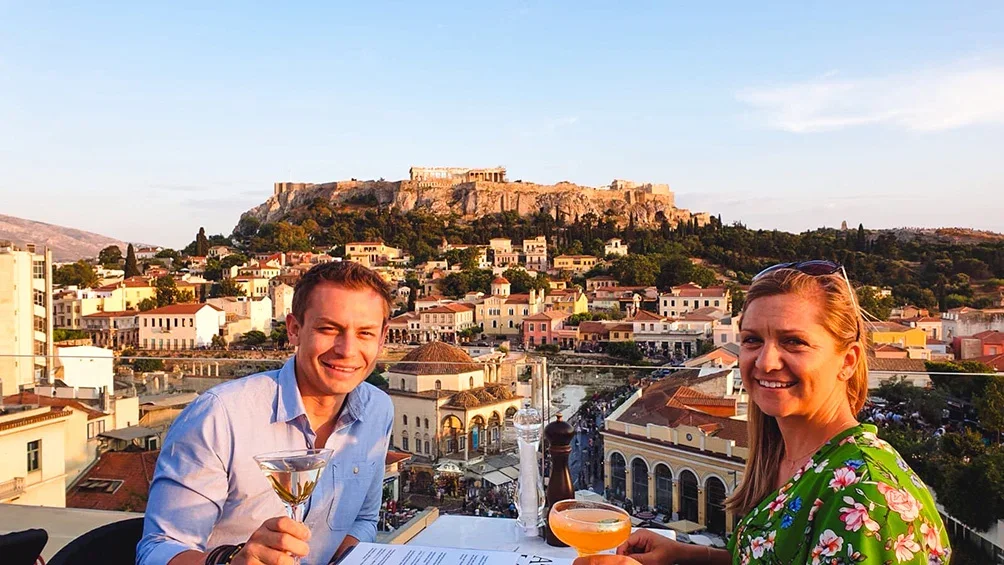 Image description: Couple having cocktails on rooftop with view of Athens, Greece.