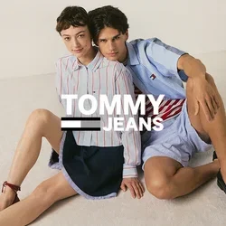 Due giovani persone sono sedute sul pavimento appoggiate l'una all'altra, indossando camicie a righe casual, pantaloncini e mocassini.