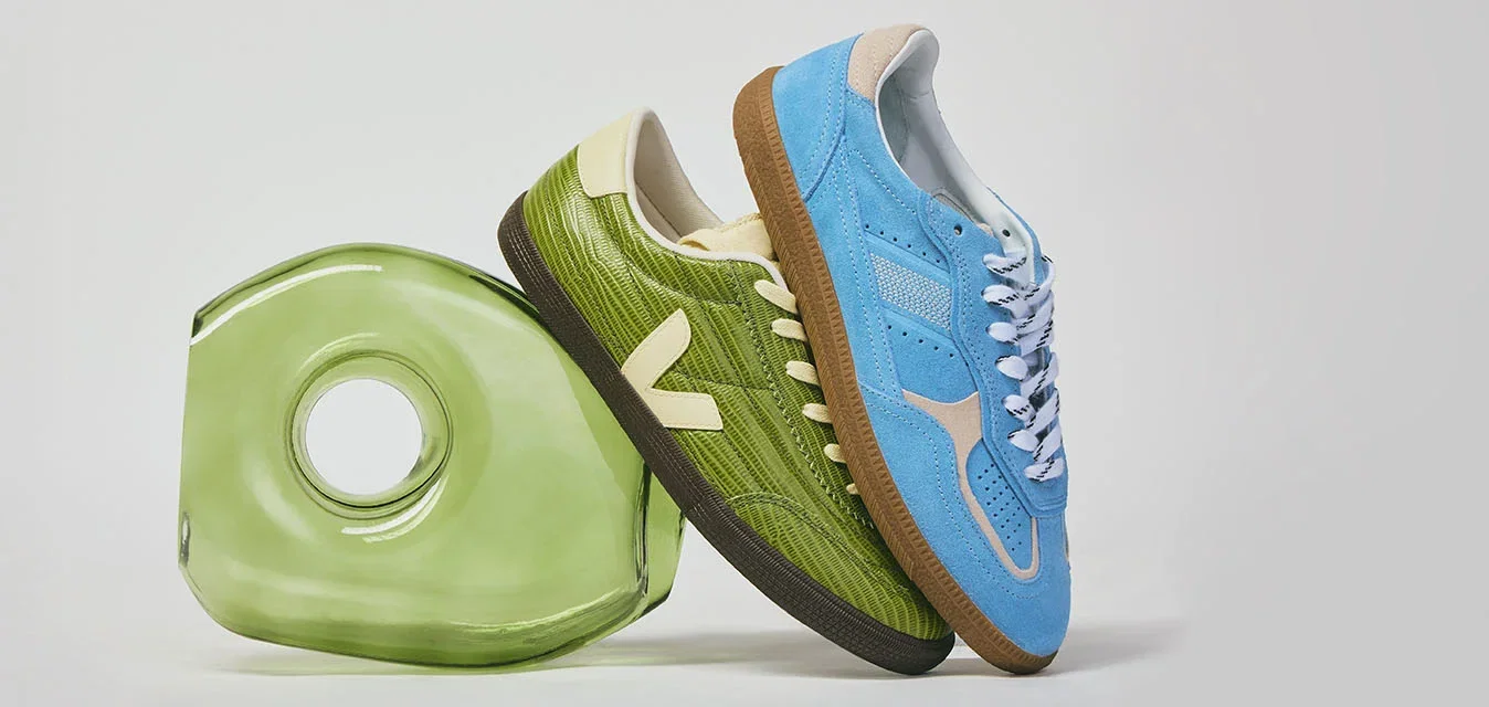 Coppia di sneaker, una verde e una blu, appoggiate a un oggetto circolare traslucido verde su sfondo bianco.