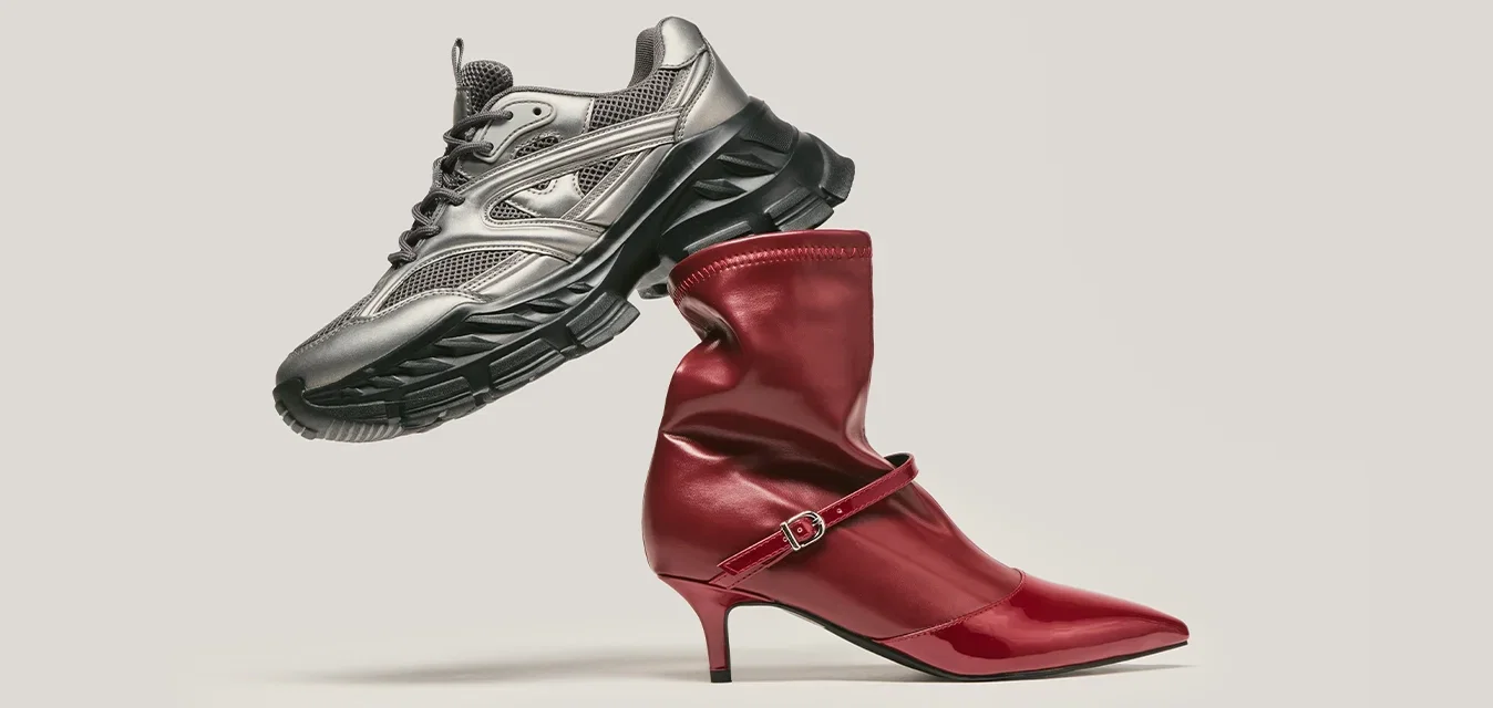 Scarpa da running grigia metallica bilanciata sopra un stivale alto in pelle rossa con cinturino, posizionata su uno sfondo chiaro e semplice.