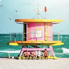 Colorful lifeguard stand on Miami Beach with people relaxing nearby.