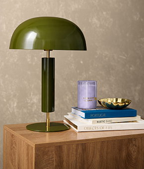A green table lamp sitting on a sideboard alongside some books and a candle.