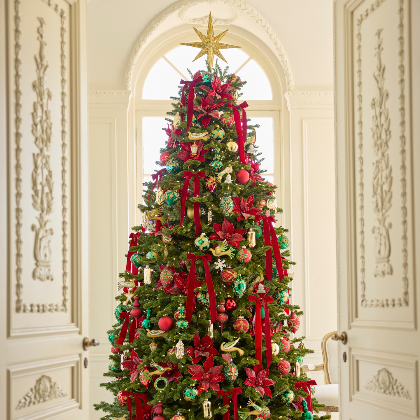 Decorated Christmas Tree with a gold star tree topper, red ribbons, red poinsettia tree picks, green and gold ornaments