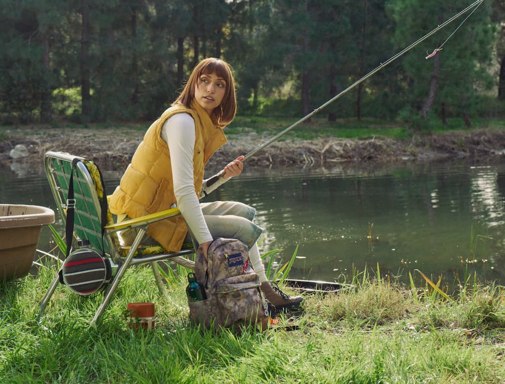 JanSport Bogcore Camo backpack next to a woman in a yellow gilet fishing