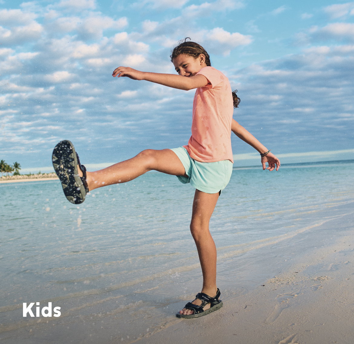 A girl playing on the beach, kicking up water.